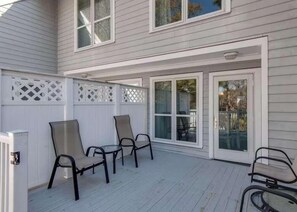 Ein überdachter Patio mit zwei Stühlen und einem Tisch, ein weißes Gitterzaun und eine Schiebetür.