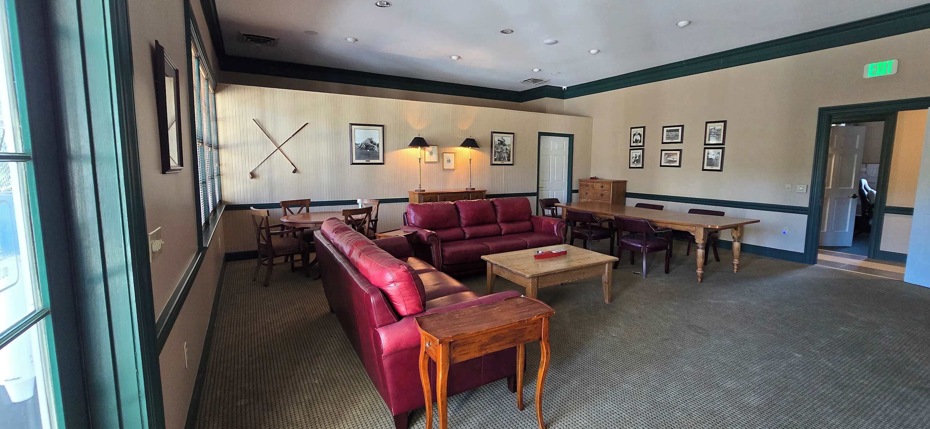 Een hotellobby met een rode leren bank, houten tafels en ingelijste foto's aan de muur.