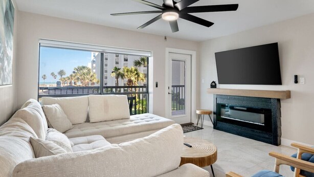 A modern living room with a sectional sofa, a fireplace, a flat-screen TV, and a ceiling fan. - Serene Oceanview Haven Designer Coastal Living (South Padre Island)