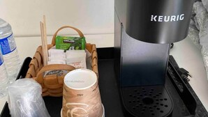 En Keurig-kaffemaskine på en bakke med en McDonald's-kop, en vandflaske og en kurv med en grøn te-pose og en kaffekop.