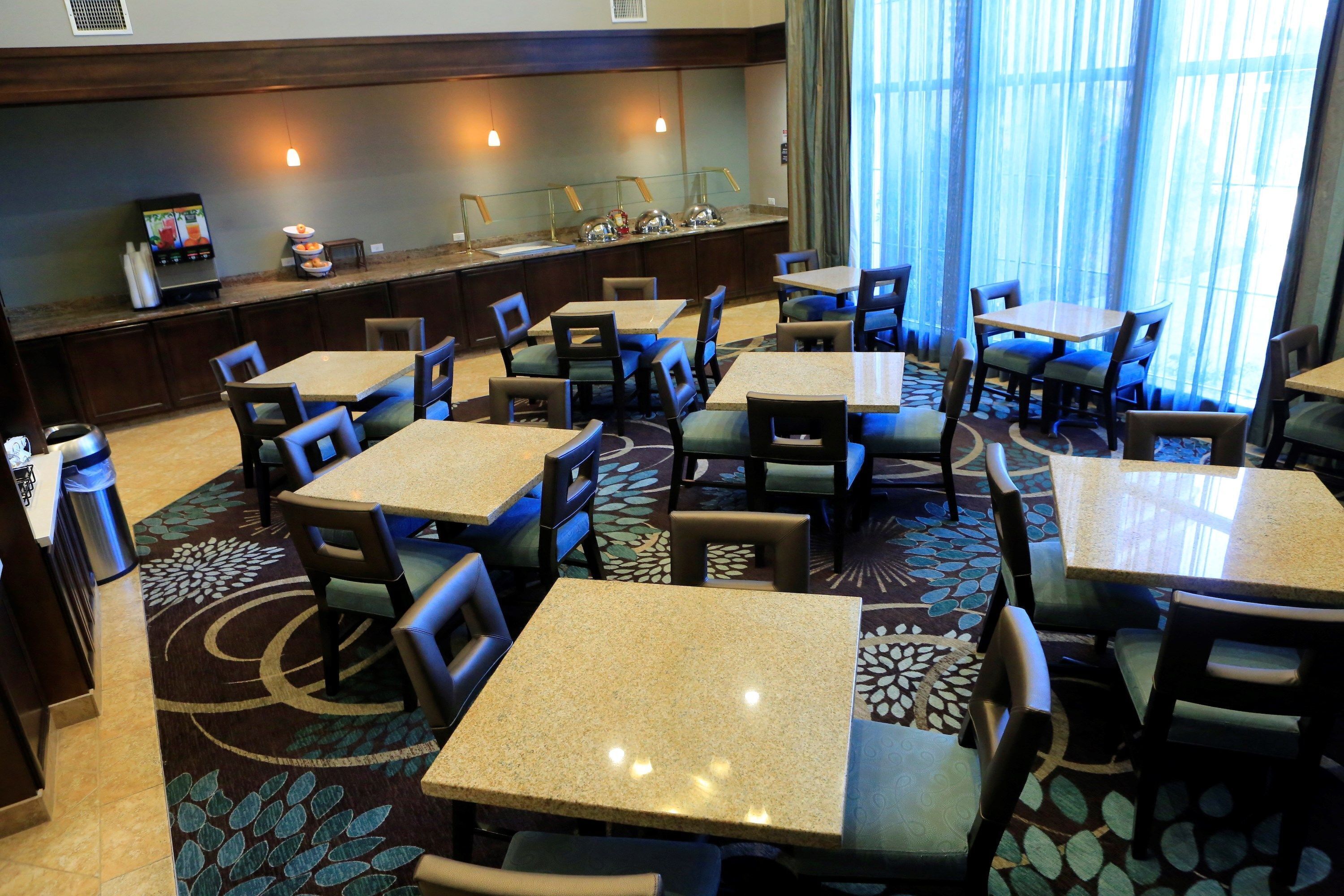 A hotel dining area with multiple tables and chairs, a counter with a television, and a patterned carpet.