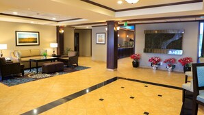 A lobby with a sofa, chairs, a coffee table, a reception desk, and potted plants.