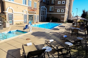 A pool area with lounge chairs and umbrellas, surrounded by a building with balconies and large windows.