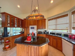 A kitchen with wooden cabinets, a central island, a microwave, and a window with blinds.
