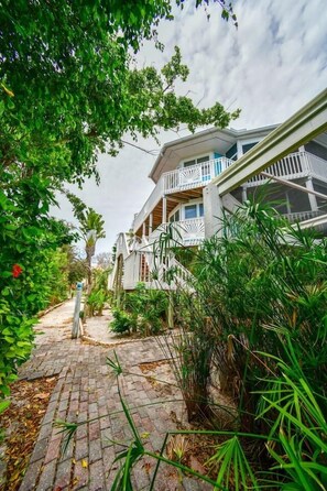 A pathway leading to a building with a white exterior and balconies, surrounded by lush greenery.
