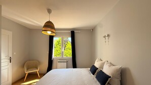 Une chambre à coucher comprenant un lit, une chaise, une fenêtre avec des rideaux, un luminaire fixé au mur et un luminaire au plafond.