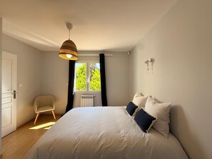 A bedroom with a bed, a chair, a window with curtains, a wall-mounted light, and a ceiling light. - Villa Romarin - Family home in the heart of the southern Mediterranean (Narbonne)