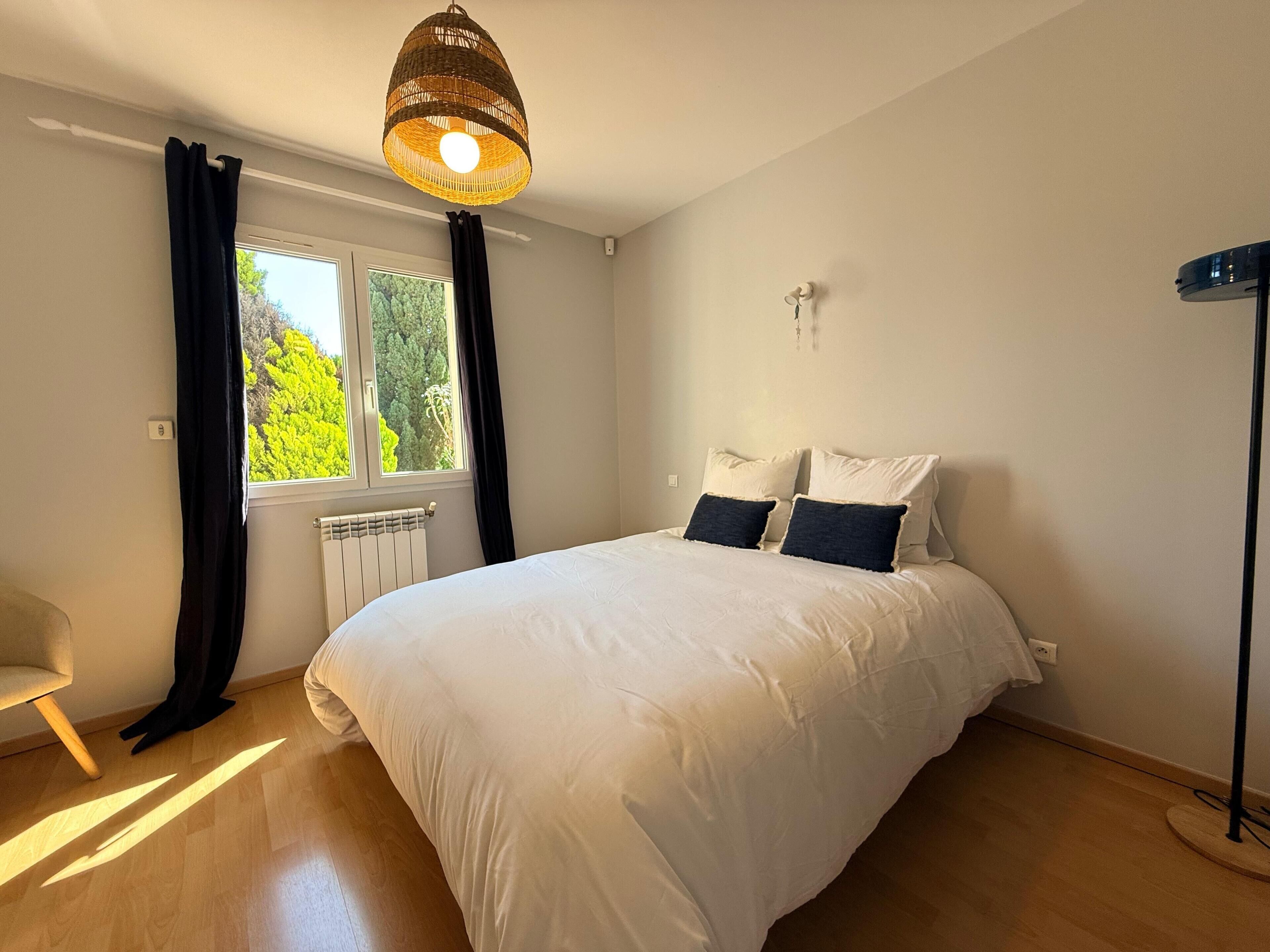 Une chambre à coucher avec un lit, une fenêtre avec des rideaux, un radiateur et une lampe sur pied.