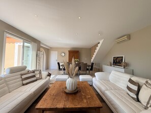 A modern living room with a wooden coffee table, white sofas, a dining area with a chandelier, and a staircase leading to an upper level. - Villa Romarin - Family home in the heart of the southern Mediterranean (Narbonne)