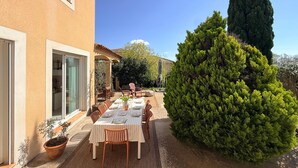 Une terrasse avec une table dressée pour le repas, entourée de plantes en pot et d’un grand arbre.