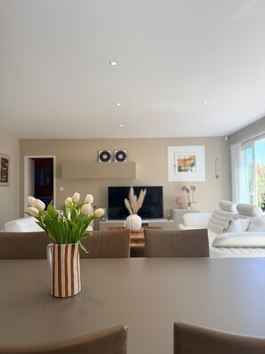 A modern living room with a dining area, a flat-screen TV, and a large window. - Villa Romarin - Family home in the heart of the southern Mediterranean (Narbonne)