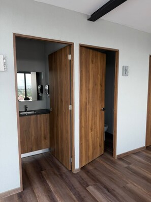 Una habitación con una puerta de madera que da a un baño y una kitchenette con un lavabo y un espejo.