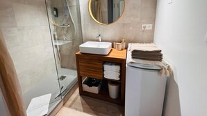A modern bathroom with a glass shower enclosure, a white sink, wooden vanity, and a round mirror. - Beautiful Apart 40 m2 garden view Large swimming pool (Saint-François)