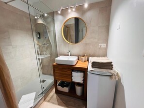 A modern bathroom with a glass shower enclosure, a white sink, wooden vanity, and a round mirror. - Beautiful Apart 40 m2 garden view Large swimming pool (Saint-François)