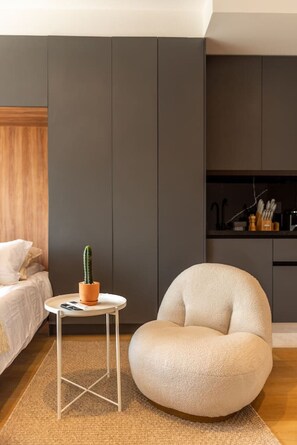 A modern bedroom with a bed, a round armchair, a small side table with a cactus, and a kitchen area in the background. - OH | Amazing Loft Roma Nte w/ AC balcony & rooftop (Mexico City)