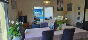 Un comedor con una mesa, sillas, un jarrón con flores, un televisor y vistas a una piscina y zona de estar al aire libre.