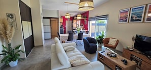 A modern living room with a sofa, a TV, and a dining area with chairs and a table. - Villa with indoor pool 150m from the beach (Plounéour-Brignogan-plages)