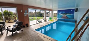 A modern indoor pool area with a clear view of the outdoors, including a garden and a distant island. - Villa with indoor pool 150m from the beach (Plounéour-Brignogan-plages)