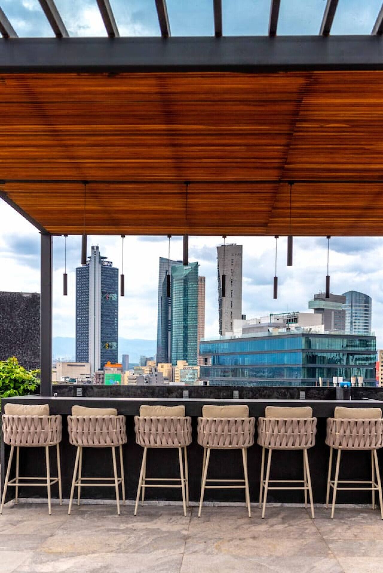 Zona de bar al aire libre cubierta con vista al horizonte de la ciudad, con edificios modernos y cielo despejado.
