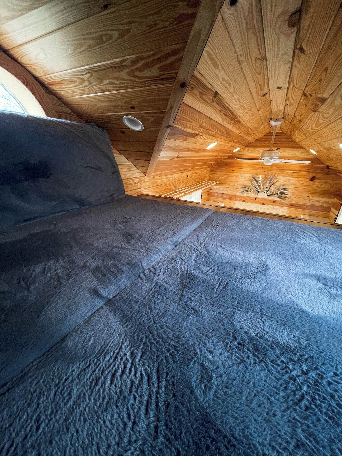 A room with a wooden ceiling, a ceiling fan, and a window.