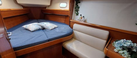 A compact cabin with a bed, a cushioned bench, a small table with a plant, and a window.