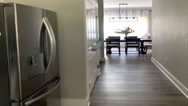 A hallway with a stainless steel refrigerator, a dining area with a table and chairs, and a light fixture above the table.