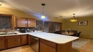 A kitchen with wooden cabinets, a central island, a dining area with a table and chairs, and pendant lighting.