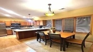 A kitchen with wooden cabinets, a central island, and a dining area with chairs and a table.