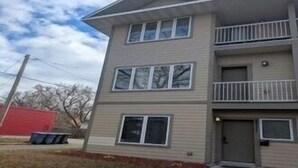 A two-story building with a balcony on the second floor, a garage door, and a small front yard.