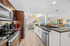 A modern kitchen with stainless steel appliances, a dining area with a chandelier, and a view of the outdoors through large windows. - Slip into island time the moment you arrive at Poppy’s Paradise (Captiva)