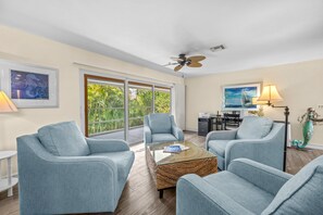 A spacious living room with two light blue armchairs, a glass coffee table, and a ceiling fan. - Slip into island time the moment you arrive at Poppy’s Paradise (Captiva)
