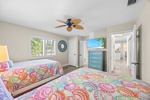A bedroom with two beds, a ceiling fan, a television, and a view of the hallway. - Slip into island time the moment you arrive at Poppy’s Paradise (Captiva)