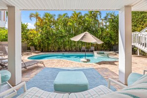 A pool area with lounge chairs, a covered seating area, and a view of palm trees. - Slip into island time the moment you arrive at Poppy’s Paradise (Captiva)
