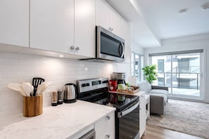 A modern kitchen with white cabinets, a built-in microwave, and a coffee maker. - New Suite • Near DT Stampede• UG Park • Banff Pass (Calgary)