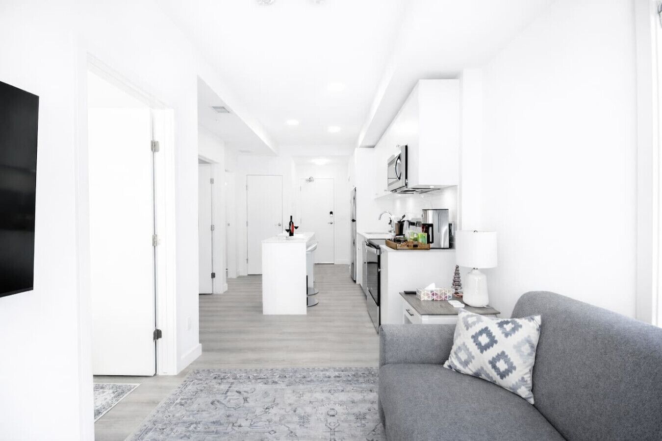 Ein moderner, minimalistischer Wohnraum mit grauem Sofa, einer kleinen Küchenzeile und einer zentralen Kochinsel.