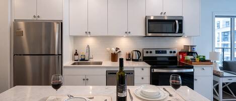 A modern kitchen with stainless steel appliances, white cabinetry, and a dining area set for two with wine glasses and a bottle.