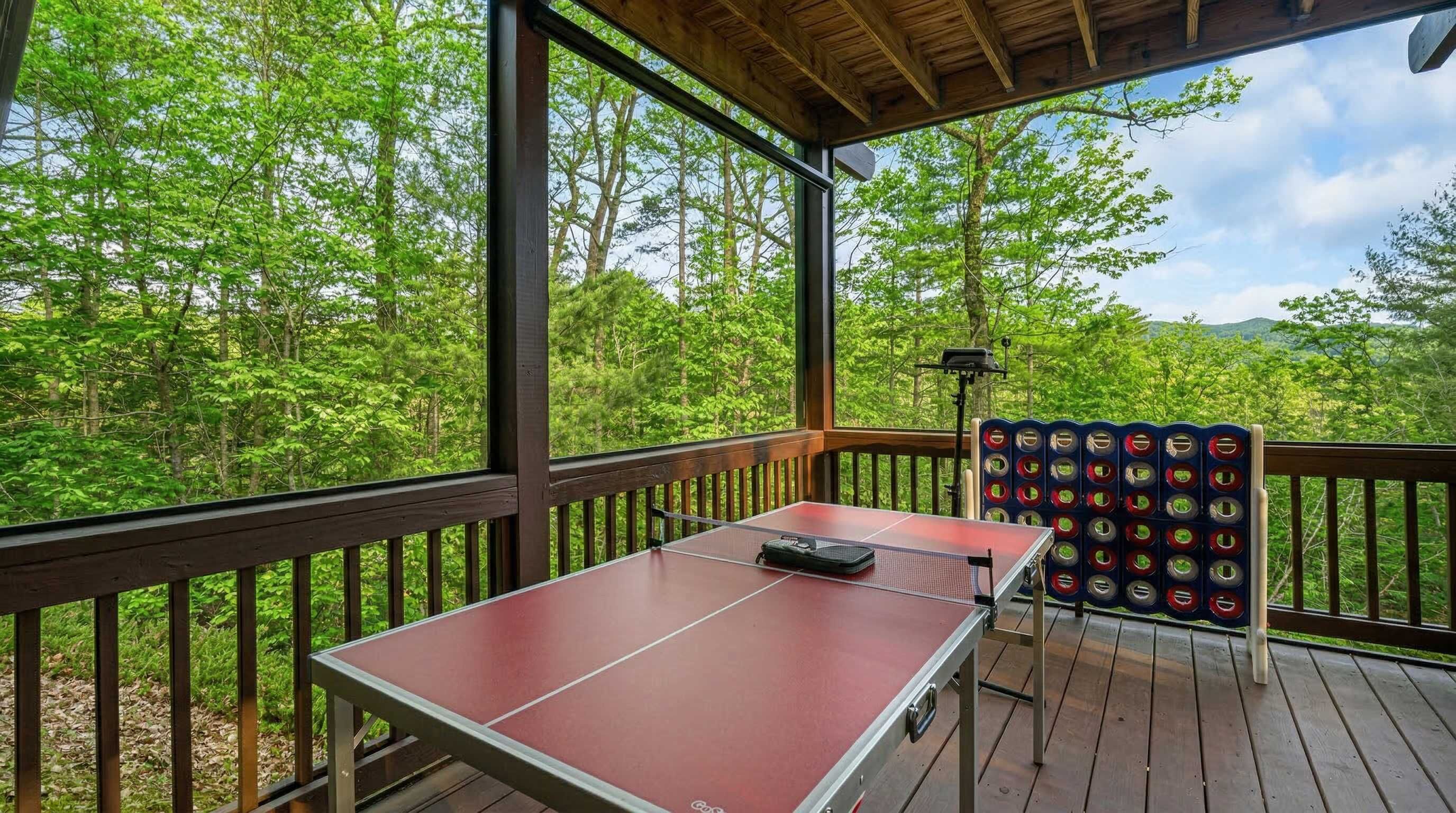 An outdoor ping pong table on a wooden deck with a view of a forest and mountains.