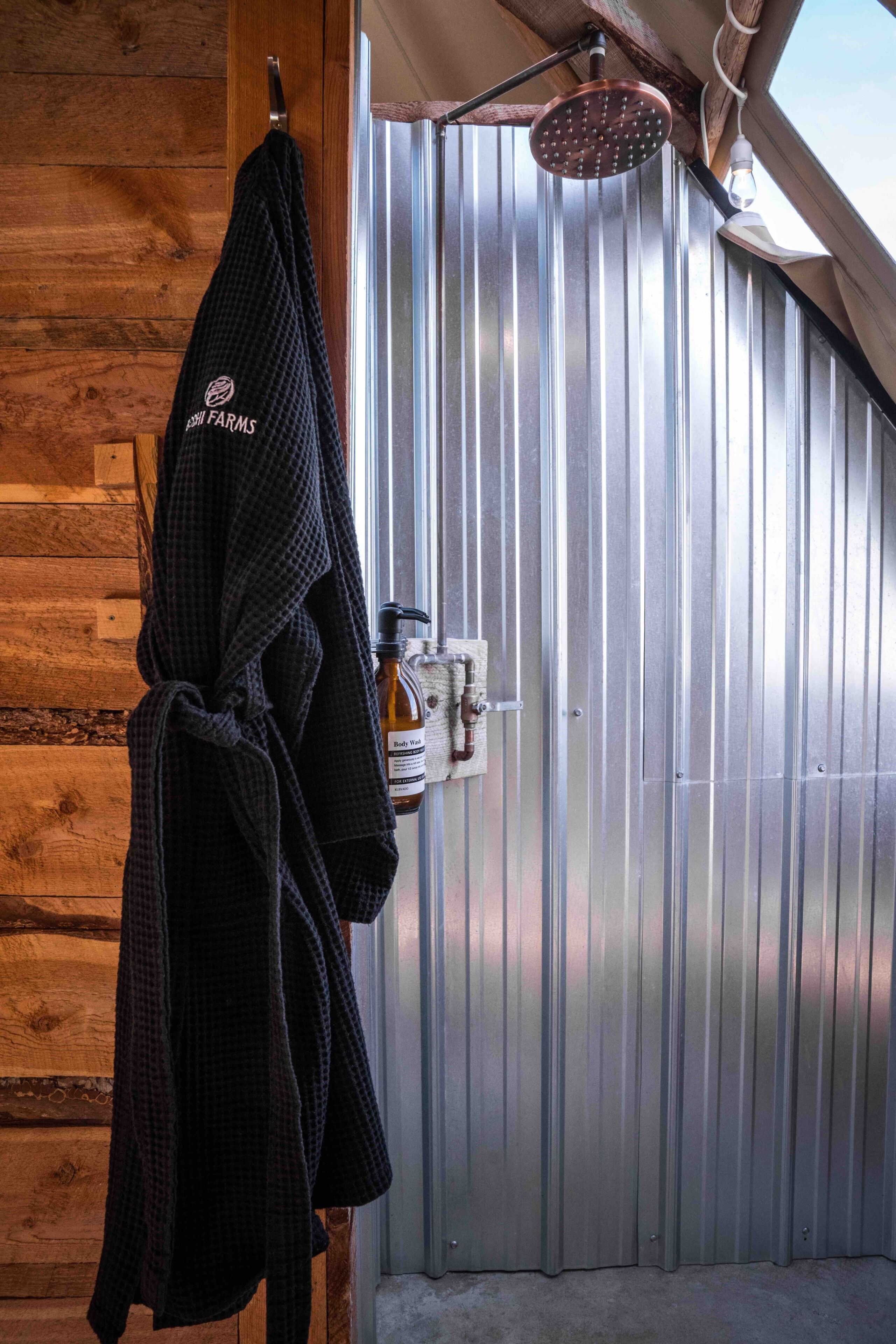A bathroom with a wooden wall, a towel hanging, a shower head, and a bottle of body spray.