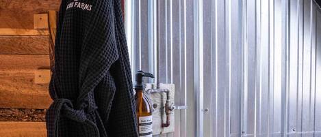 A bathroom with a wooden wall, a towel hanging, a shower head, and a bottle of body spray.