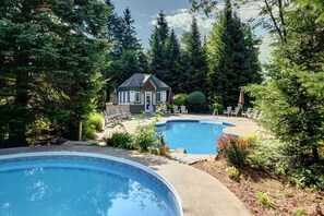 Ein Poolbereich mit zwei Pools, einem kleinen Gebäude und umliegenden Bäumen.
