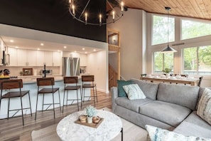 Eine moderne Küche mit weißen Schränken, eine Essecke mit grauem Sofa und ein großes Fenster für natürliches Licht.
