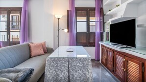 A living room with a sofa, a glass-top coffee table, a TV on a wooden cabinet, and purple curtains. - Apartment 'Mia' with Wi-Fi and Air Conditioning (Ronda)