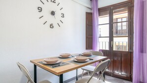 A dining area with a wooden table, four chairs, a wall clock, and a window with purple curtains. - Apartment 'Mia' with Wi-Fi and Air Conditioning (Ronda)