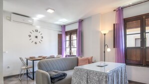 A room with a sofa, a table with a patterned tablecloth, a clock on the wall, and purple curtains. - Apartment 'Mia' with Wi-Fi and Air Conditioning (Ronda)