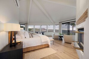 Een slaapkamer met een groot bed, een nachtkastje, een lamp, een stoel, een klein tafeltje en uitzicht op het groen.