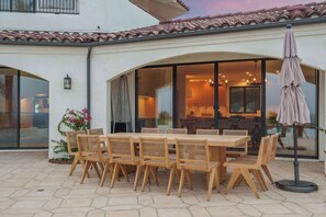 Une terrasse extérieure avec une table et des chaises en bois, une porte vitrée donnant sur une pièce et un parasol de terrasse.