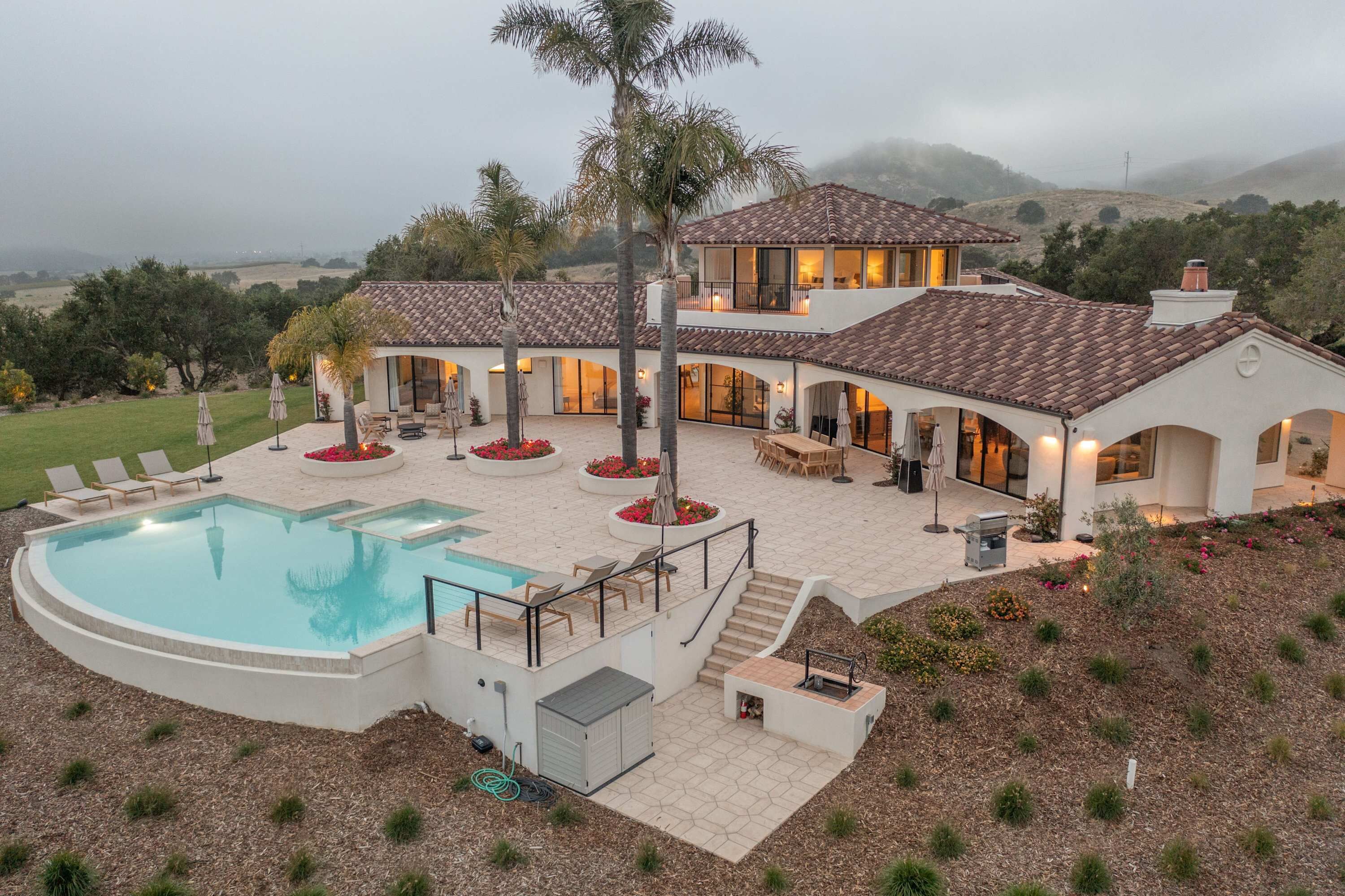 A two-story house with a swimming pool, outdoor seating, and a view of the surrounding landscape.