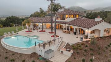 A two-story house with a swimming pool, outdoor seating, and a view of the surrounding landscape.