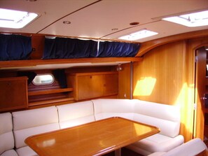 A cabin with a white cushioned bench, a wooden table, and a window with curtains. - Sun-Kissed Sailing Adventure in Islas Sarónicas (Alimos)