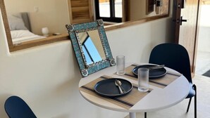 Zona pranzo con un tavolo rotondo, due sedie, uno specchio con cornice decorativa e una finestra con persiane.